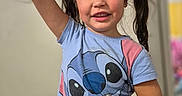 Alana joined the competition — help win amazing prizes! child, girl, smiling, portrait, indoors, standing, raised_arm, pigtails, hair_bows, blue_shirt, stitch_character, black_shorts, wood_floor, home, playful, happy, face, person, casual_clothing, colorful_background