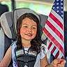 Alana is registered to the contest to win money with this photo: child, girl, smiling, car_seat, vehicle, american_flag, flag, patriotic, portrait, sitting, seatbelt, harness, indoor, birthday_bag, colorful, dress, long_hair, happy, passenger, family_trip