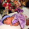 Mia is registered to the contest to win money with this photo: baby, newborn, sleeping, lavender_outfit, headband, flowers, plush_doll, purple_dress, balloons, white_blanket, carpet, indoors, cute, peaceful, child, portrait, soft_lighting, decor, toy, colorful