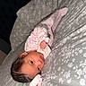 Mia is registered to the contest to win money with this photo: baby, infant, newborn, bed, blanket, floral, onesie, pattern, sleepwear, face, head, person, skin, hair, lying_down, cute, indoors, comfort, soft, young_child