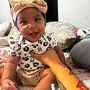 Magnolia joined the competition — help win amazing prizes! baby, infant, smiling_baby, headband, bow, onesie, leopard_print, hand, adult_arm, tattoo, pacifier, pillow, blanket, bed, toes, plush_toy, person, portrait, happy, indoors