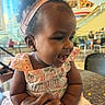 baby, child, infant, smiling, laughing, portrait, close_up, headband, earring, dress, floral_pattern, sitting, adult_hand, indoors, mall, cafe, escalator, chair, bokeh, happy
