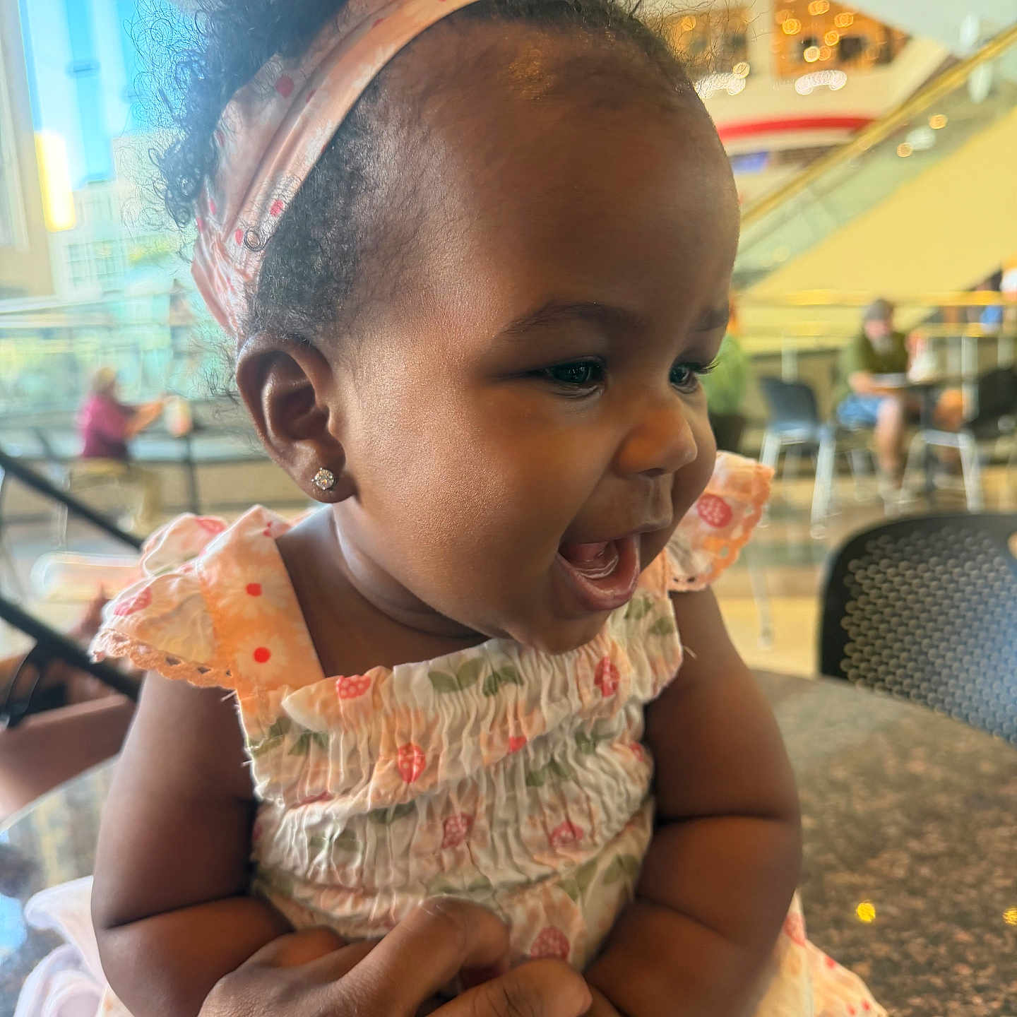 Imanialay joined the competition — help win amazing prizes! baby, child, infant, smiling, laughing, portrait, close_up, headband, earring, dress, floral_pattern, sitting, adult_hand, indoors, mall, cafe, escalator, chair, bokeh, happy