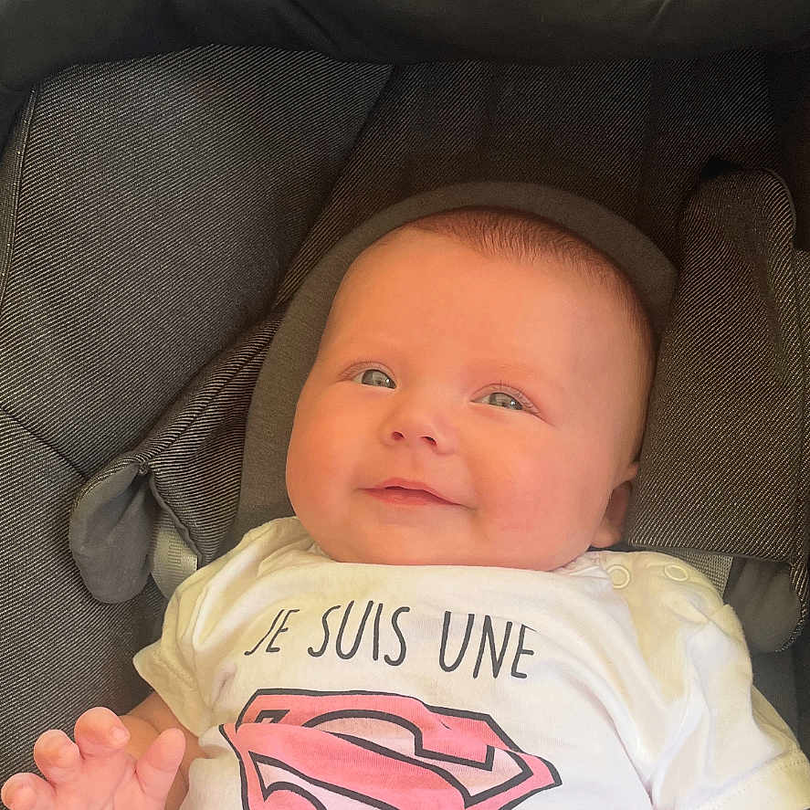 Eden a rejoint le concours — aidez-le/la à gagner de superbes lots ! baby, car_seat, child, clothing, comfort, cute, fabric, greenery, hand, happy, infant, outdoor, pink, portrait, seat, smiling, superman_logo, toddler, white_shirt, young_child