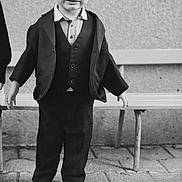 Nino a rejoint le concours — aidez-le/la à gagner de superbes lots ! child, boy, suit, jacket, vest, shirt, white_shoes, outdoor, pavement, bench, wall, portrait, standing, smiling, formal_clothing, young, person, monochrome, black_and_white, cute