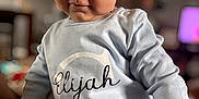 Elijah joined the competition — help win amazing prizes! baby, child, infant, face, expression, clothing, sitting, indoor, person, cute, portrait, long_sleeve, onesie, light_blue, curious, smirk, head, skin, eyes, young