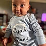 baby, child, infant, face, expression, clothing, sitting, indoor, person, cute, portrait, long_sleeve, onesie, light_blue, curious, smirk, head, skin, eyes, young