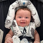 Robert is registered to the contest to win money with this photo: baby, smile, infant, car_seat, blanket, head_support, clothing, happy, child, cute, face, hand, fabric, pattern, comfort, seatbelt, indoors, portrait, skin, young_child