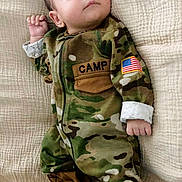 Leon joined the competition — help win amazing prizes! baby, infant, camouflage, clothing, boots, blanket, lying_down, face, person, cute, young_child, portrait, soft_texture, indoors, sleepwear, military_style, hand, expression, small, newborn