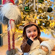 Mila participe au concours pour gagner de l'argent avec cette photo : baby, child, reindeer_costume, doll, christmas_tree, holiday, festive, gnome, toy, smile, cute, indoors, decorations, warm_lighting, floor, cozy, seasonal, cute_expression, portrait, holiday_spirit