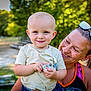 Logan is registered to the contest to win money with this photo: child, toddler, woman, smile, outdoor, sunlight, greenery, pacifier, casual_clothing, sunglasses, portrait, holding, happy, nature, daylight, headwear, person, skin, hair, park