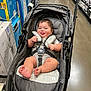 Gabriel is registered to the contest to win money with this photo: baby, stroller, child, smiling, tongue_out, shopping_aisle, boxes, floor, gray, seat_belt, infant, happy, retail, store, person, cart, clothing, foot, head, cute