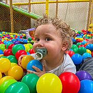 Malone participe au concours pour gagner de l'argent avec cette photo : toddler, child, pacifier, ball_pit, colorful_balls, curly_hair, indoor_playground, play_area, baby, bright_colors, smiling, fun, cute, young_child, clothing, hand, face, person, play, happy