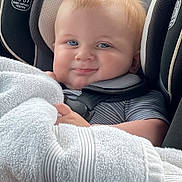 Bryson is registered to the contest to win money with this photo: baby, child, car_seat, seatbelt, blue_eyes, blond_hair, towel, smile, cute, infant, striped_clothing, safety, indoors, closeup, face, headrest, comfort, car_interior, soft_texture, happy