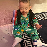 Toni participe au concours pour gagner de l'argent avec cette photo : car_prints, child, colorful_clothing, cute, floor, footwear, happy, indoor, laughing, motion_blur, pajamas, patterned_rug, playful, rug, sitting, smiling, toddler, toy, white_shoes, young_child