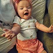 Sophia is registered to the contest to win money with this photo: baby, child, pink_bow, headband, shorts, white_shirt, pillow, blanket, smiling, happy, reaching_out, indoor, cute, infant, person, portrait, soft_lighting, couch, relaxed, clothing