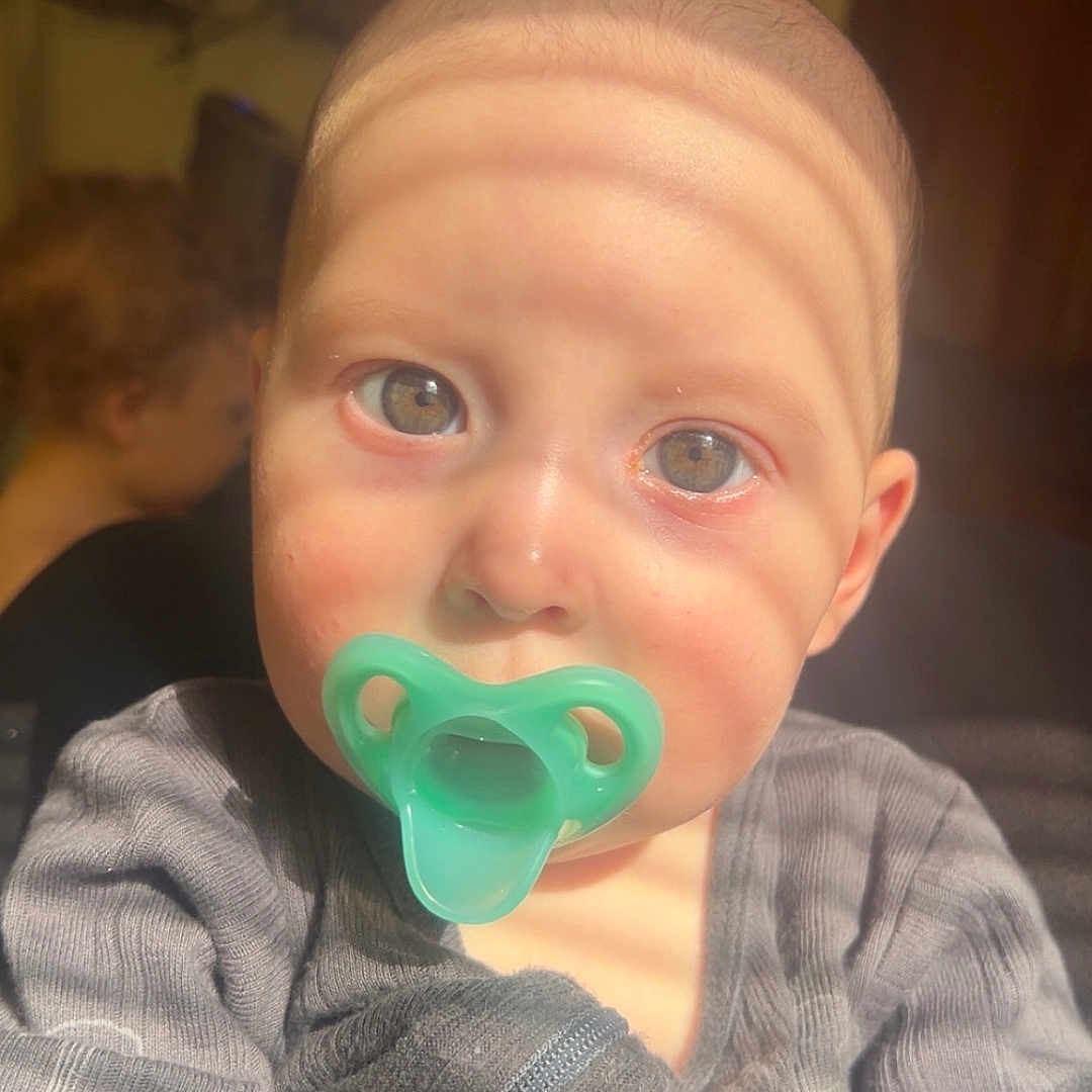 Weston is registered to the contest to win money with this photo: accessories, baby, beverage, bodypart, clothing, coffee, coffeecup, couch, ear, face, finger, furniture, hand, head, person, photography, portrait, shirt, t_shirt, toy