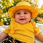 Elianna is registered to the contest to win money with this photo: baby, child, yellow_hat, yellow_clothing, smiling, outdoor, flower_garden, blanket, sunlight, happy, portrait, cute, nature, summer, greenery, toddler, face, headwear, sitting, bright