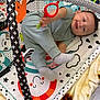 Aaron is registered to the contest to win money with this photo: baby, play_mat, toy, red_ring, socks, clothing, infant, child, face, hand, footwear, patterned_mat, colorful, playtime, smiling, indoors, soft_blanket, baby_gym, cute, tongue_out