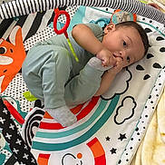Aaron joined the competition — help win amazing prizes! baby, child, infant, play_mat, sock, chewing, rainbow, stars, toy, blanket, cute, smiling, lying_down, colorful, soft_toy, person, indoors, clothing, happy, playtime