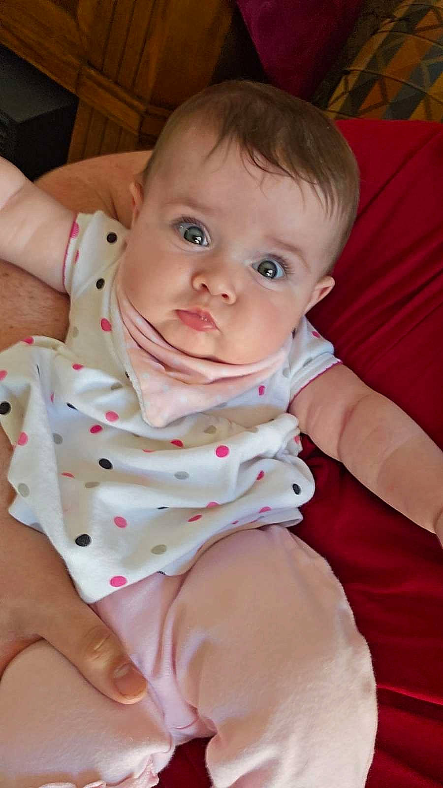 Arleigh is registered to the contest to win money with this photo: arm, baby, baby_toddler_clothing, cheek, child, collar, comfort, elbow, finger, happy, human_leg, linens, pattern, person, sitting, skin, sleeve, stomach, thigh, thumb