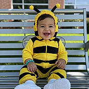 Liam joined the competition — help win amazing prizes! baby, child, costume, bee_costume, smiling, bench, outdoor, happy, cute, footwear, white_shoes, bracelet, person, portrait, infant, yellow, black, headgear, playful, sitting