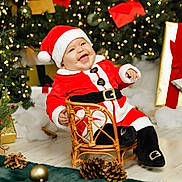 Liam joined the competition — help win amazing prizes! baby, child, santa_claus_costume, christmas_tree, holiday_lights, gift_box, pine_cones, wicker_chair, festive, smiling, indoor, celebration, red_hat, red_clothing, black_boots, decorations, seasonal, happy, portrait, holiday