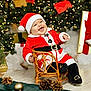 baby, child, santa_claus_costume, christmas_tree, holiday_lights, gift_box, pine_cones, wicker_chair, festive, smiling, indoor, celebration, red_hat, red_clothing, black_boots, decorations, seasonal, happy, portrait, holiday