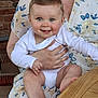Alban a rejoint le concours — aidez-le/la à gagner de superbes lots ! baby, child, person, blue_eyes, white_onesie, smiling, sitting, hand, lap, floral_clothing, table, wooden_table, brick_wall, indoor, happy, cute, skin, face, short_hair, holding