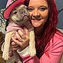 woman, dog, pet, indoor, pink_clothing, hat, smile, red_hair, holding, cute, puppy, sweater, face, hand, human, fur, animal, friendship, joy, companion