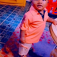Braylen is registered to the contest to win money with this photo: casual_clothing, child, curious, floor, furniture, home, indoor, orange_shirt, person, portrait, rug, shorts, sneakers, standing, table, tile_floor, toddler, toy_car, wooden_cabinet, young_child