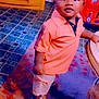 casual_clothing, child, curious, floor, furniture, home, indoor, orange_shirt, person, portrait, rug, shorts, sneakers, standing, table, tile_floor, toddler, toy_car, wooden_cabinet, young_child