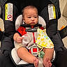 baby, infant, car_seat, bottle, blanket, clothing, foot, hand, face, person, indoor, flooring, safety_harness, pacifier, red_clothing, black_car_seat, cute, child, newborn, baby_accessory