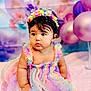 baby, child, pastel_colors, rainbow_dress, tulle, headband, floral, balloons, pink_blanket, curious_expression, indoor, portrait, cute, soft_lighting, celebration, decorations, sitting, young_child, colorful, adorable