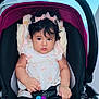 baby, child, stroller, toy, bow, hair, face, hand, clothing, sitting, seat_belt, infant, cute, indoor, portrait, colorful, pink, black, blue, expression