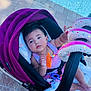 baby, stroller, poolside, toy, child, infant, purple, outdoor, curious, comfort, seat, playtime, relaxed, sunlight, pavement, summer, candid, cute, colorful, safety_belt