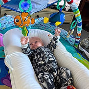 Kaladin joined the competition — help win amazing prizes! baby, infant, onesie, baby_lounger, toy_fish, play_mat, colorful, indoor, child, cute, smiling, reaching, soft_toys, patterned_clothing, cushion, furniture, floor, play_area, young_child, happy