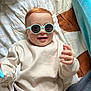 Lucien a rejoint le concours — aidez-le/la à gagner de superbes lots ! baby, child, sunglasses, smile, red_hair, sweater, bed, blanket, cozy, cute, indoor, happy, person, portrait, infant, relaxing, clothing, hand, face, fashion