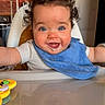 baby, bib, blue_eyes, cheeks, closeup, curly_hair, drooling, face, feeding, happy, high_chair, infant, kitchen, portrait, reflection, refrigerator, smile, sticker, table, toy
