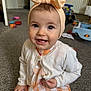 baby, child, girl, headband, bow, smile, carpet, indoor, toys, white_cardigan, dress, peach, happy, cute, person, infant, sitting, home, floor, clothing