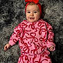 baby, child, smiling, headband, red_bow, pink_outfit, patterned_clothing, lying_down, gray_rug, fluffy_texture, cute, portrait, indoor, happy, infant, apparel, person, toddler, head, hands