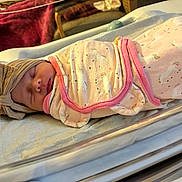 Josie is registered to the contest to win money with this photo: newborn, baby, swaddled, blanket, unicorn, rainbow, hat, sleeping, bassinet, hospital, infant, bed, clothing, cute, child, person, soft, resting, pink, cozy