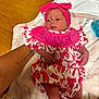 baby, newborn, infant, pink_bow, headband, dress, patterned_clothing, tattoo, arm, blanket, soft_texture, wooden_floor, person, child, cute, resting, indoor, holding, hand, skin
