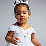 Brianna is registered to the contest to win money with this photo: toddler, child, girl, white_dress, bow, curly_hair, portrait, smiling, jewelry, necklace, bracelet, studio, pose, cute, innocent, fashion, happy, person, young, photography