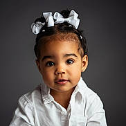 Brianna is registered to the contest to win money with this photo: toddler, child, portrait, white_bow, white_shirt, studio_lighting, curly_hair, cute, face, young_child, girl, innocent, looking_at_camera, black_hair, earrings, indoor, smiling, fashion, closeup, background