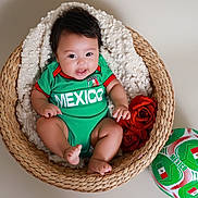 Penelope is registered to the contest to win money with this photo: baby, basket, blanket, green_clothing, mexico, red_roses, soccer_ball, smiling, cute, infant, portrait, indoors, woven_basket, happy, child, football, sports_theme, red_and_green, soft_texture, sitting