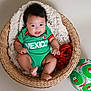baby, basket, blanket, green_clothing, mexico, red_roses, soccer_ball, smiling, cute, infant, portrait, indoors, woven_basket, happy, child, football, sports_theme, red_and_green, soft_texture, sitting