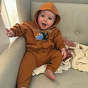 Rían joined the competition — help win amazing prizes! baby, blanket, brown_clothing, casual, child, couch, cozy, cute, fabric, face, foot, hand, happy, hoodie, indoor, infant, person, seated, smile, sofa