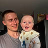 baby, child, person, man, smiling, happy, indoor, bib, clothing, facial_expression, portrait, holding, young_adult, light, face, head, cute, parent, family, home