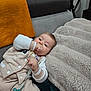 baby, infant, pacifier, pacifier_clip, blanket, plush_blanket, sofa, couch, onesie, beige_outfit, hand_in_mouth, sleepy, cozy, indoor, soft_texture, orange_towel, head, face, lying_down, portrait